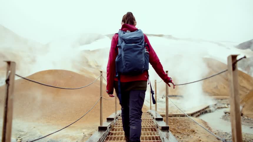 The woman hikes over the small bridge on the mountain