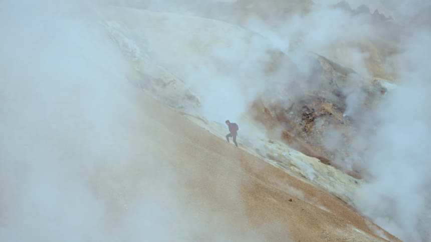 Person walks along a mountainside surrounded by fog and steam