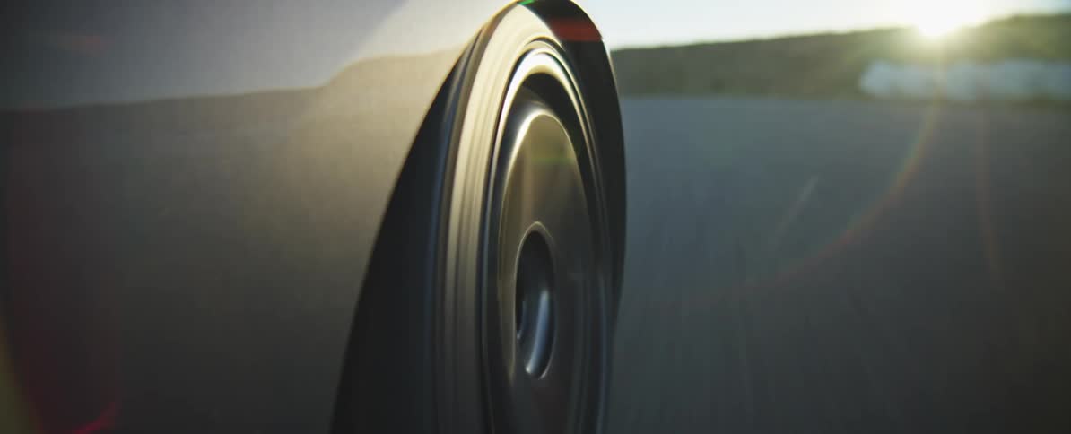 A close view of a black car wheel spinning at high speed on an asphalt road during a clear day with a blurred background of the track and horizon