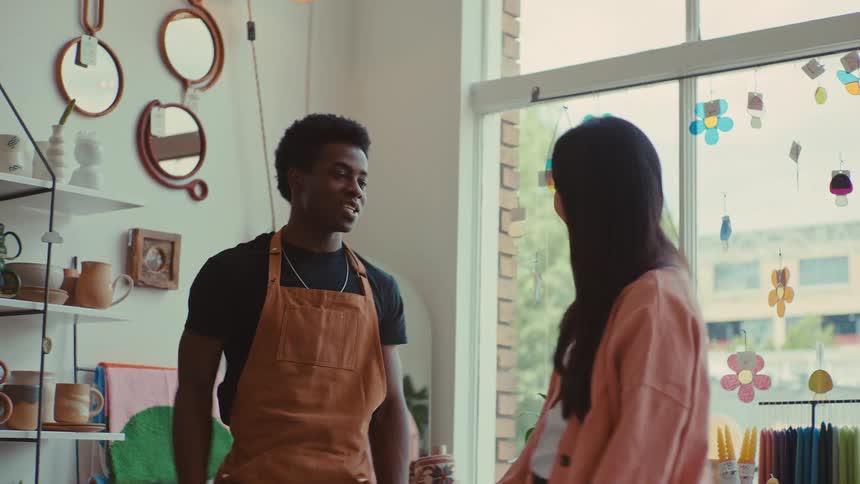 A man in an apron and a woman share a high five and smile inside a sunlit craft shop