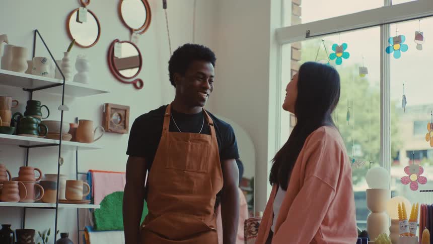 A man in an apron and a woman share a high five and smile inside a sunlit craft shop