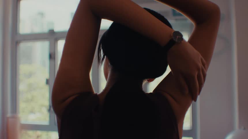 Woman performs arm stretches with arms raised near a window in a welllit environment