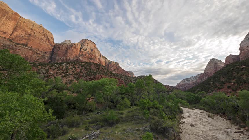 Time lapse of clouds passing over a canyon with a shallow creek and vegetation