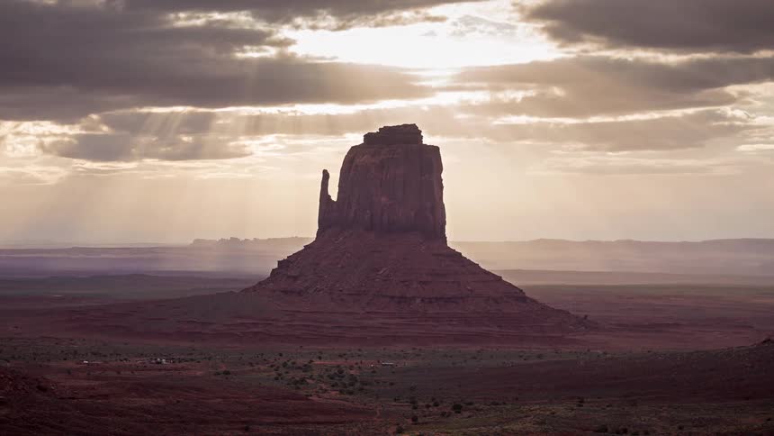 Butte rock formation on the desert landscape as clouds move across the sky