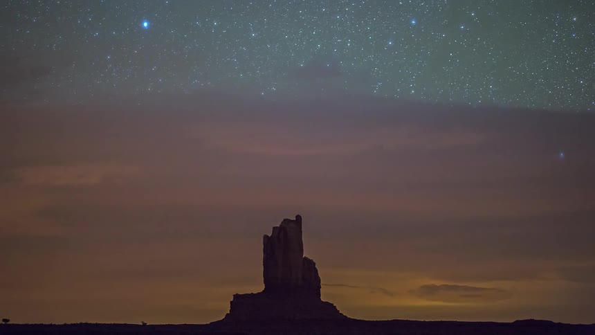 Rock formation silhouetted on the desert landscape as stars and clouds move across the sky