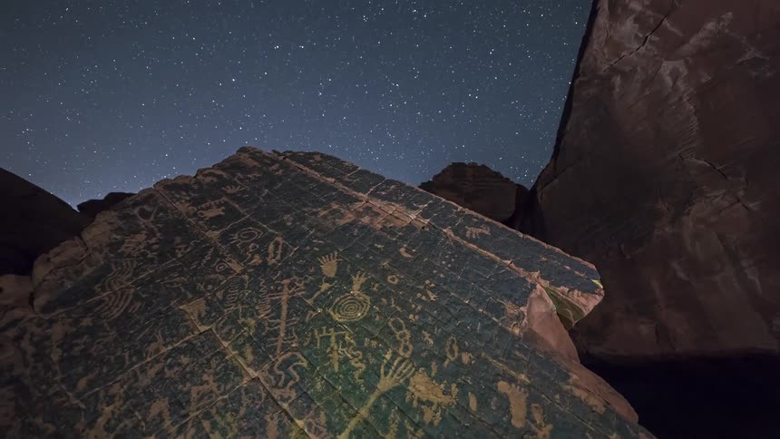 Rock panels display ancient petroglyphs under a starry night sky in an isolated canyon
