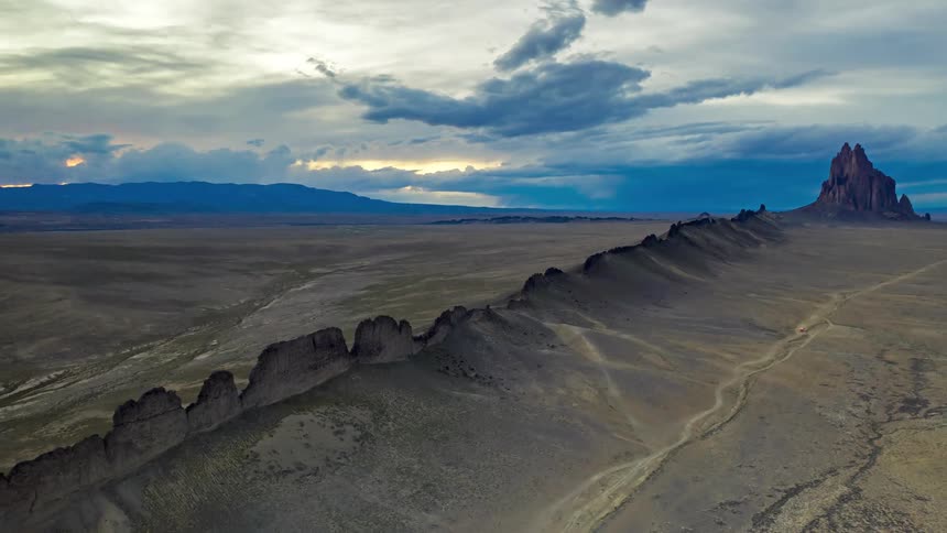 Rocky ridge stretches toward an isolated volcanic formation under a heavy sky in the new mexico desert