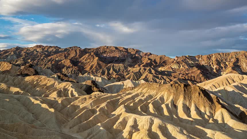 Arid mountain formations with eroded ridges under a partly cloudy sky