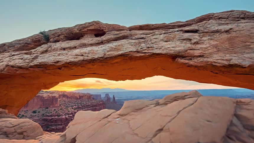 Rocky arch illuminated by golden light over an extensive canyon