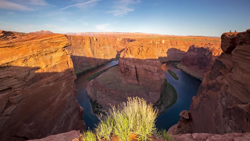 This video shows a wideangle timelapse view of horseshoe bend in arizona where the colorado river winds around a massive rock formation shadows gradually stretch across the orange canyon walls and the river below as the sun moves across the sky
