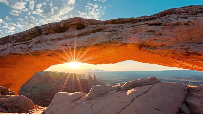 Sunrise light slips through a natural rock arch in the canyon the suns glow catching between the stone edges as it rises