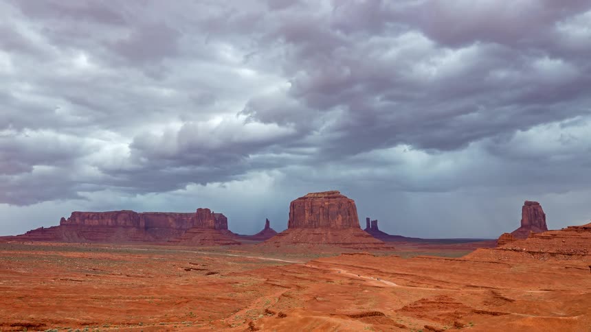 Cars travel on the road with mesa and butte red rock formations across the desert landscape