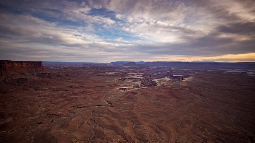 Vast desert landscape with deep canyons and rock formations under a partly cloudy sky