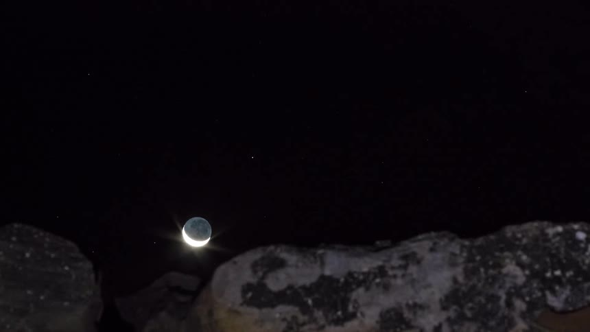 Crescent moon sets behind a mountain