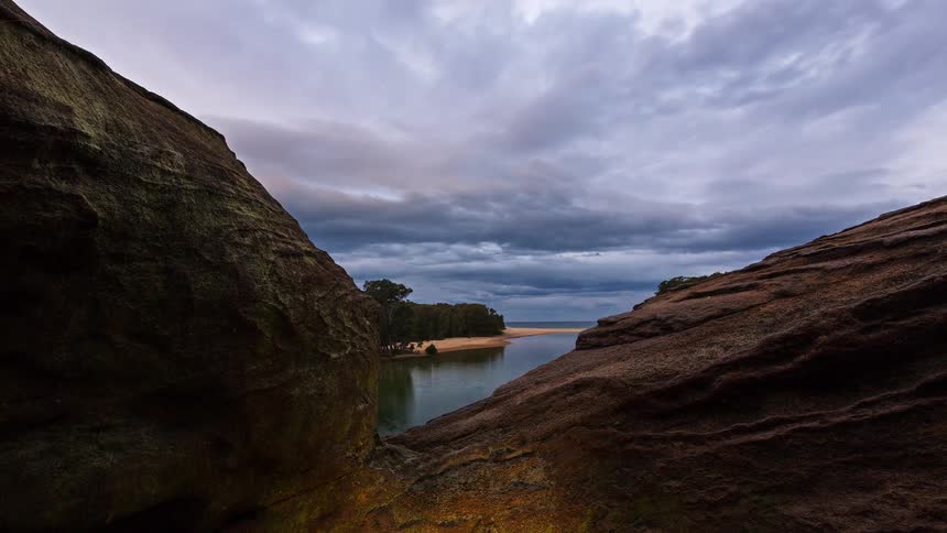 Calm river winds between rocky formations and dense vegetation under a cloudy evening sky