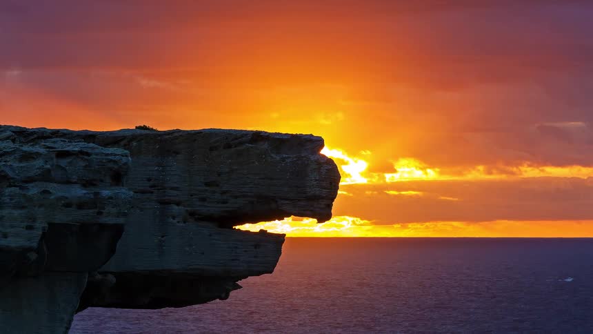 Rock formation juts over the ocean with the horizon lit by sunset