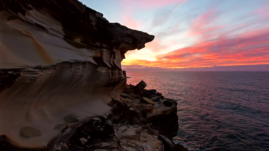 Rocky cliff by the ocean at sunset with waves hitting the shoreline