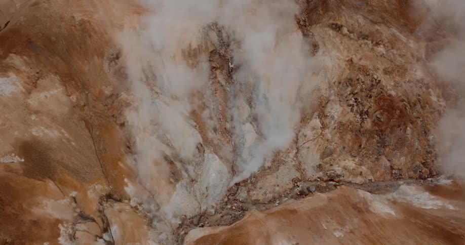 A view from above shows thick white steam rising from several vents in a steep rocky mountain with orange and brown soil
