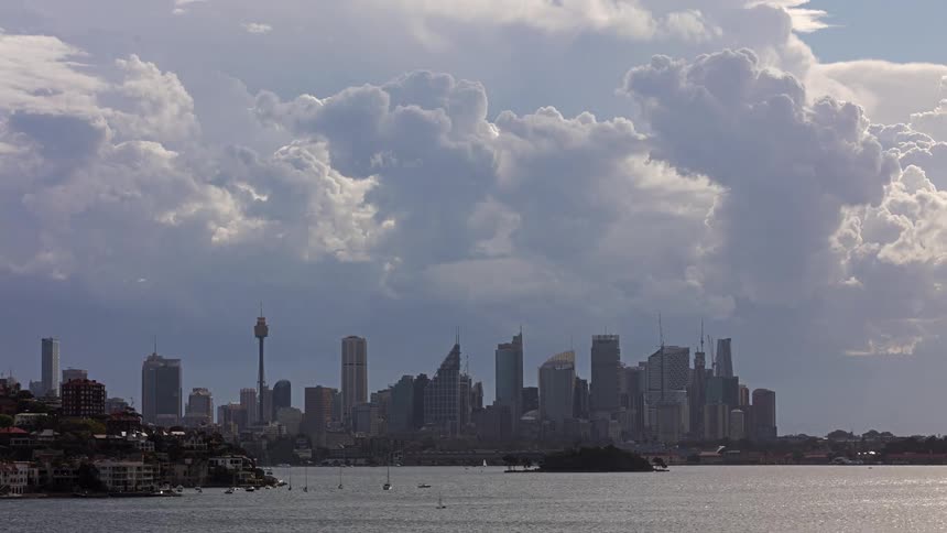 Urban skyline by the water under dense clouds and a partially lit sky