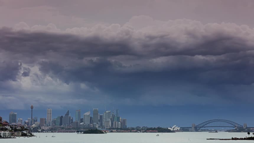 A view of the city skyline across a body of water as a large shelf cloud and dark storm clouds roll quickly over the buildings and a bridge