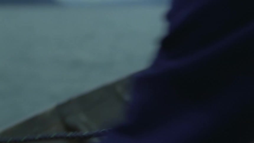 A persons hands pull a thick dark rope out of the water and over the side of a boatthe scene is set against a backdrop of calm grey water and distant misty mountains during twilight