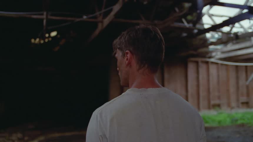 Young adult man with his face covered in dirt standing on a wooden building with mud and plants inside during day time