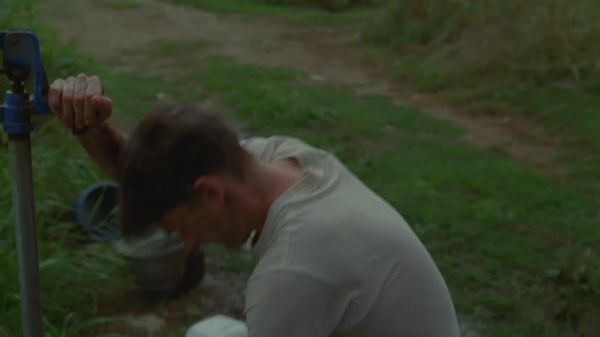 A man in the mountains shuts off a hand pump and picks up two water jugs and walks away