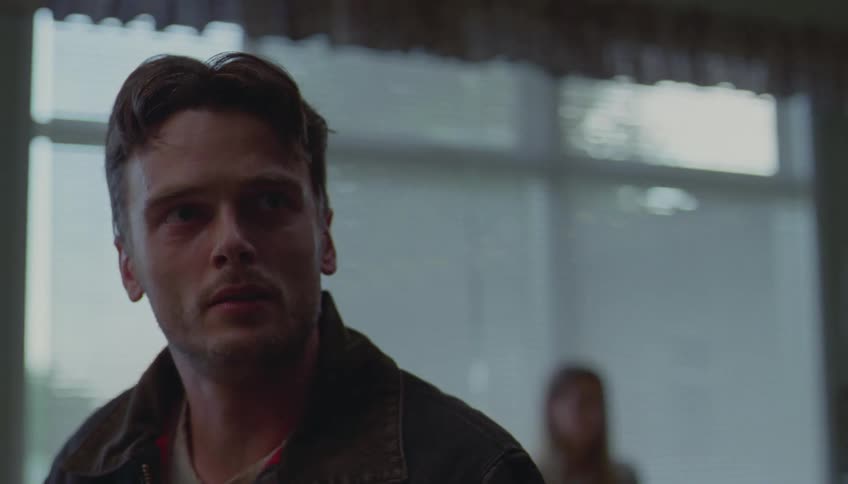 Young adult man sitting down next to a woman with a sad facial expression who stands up and walks away while he looks at a distance with a frustrated facial expression indoors during day time