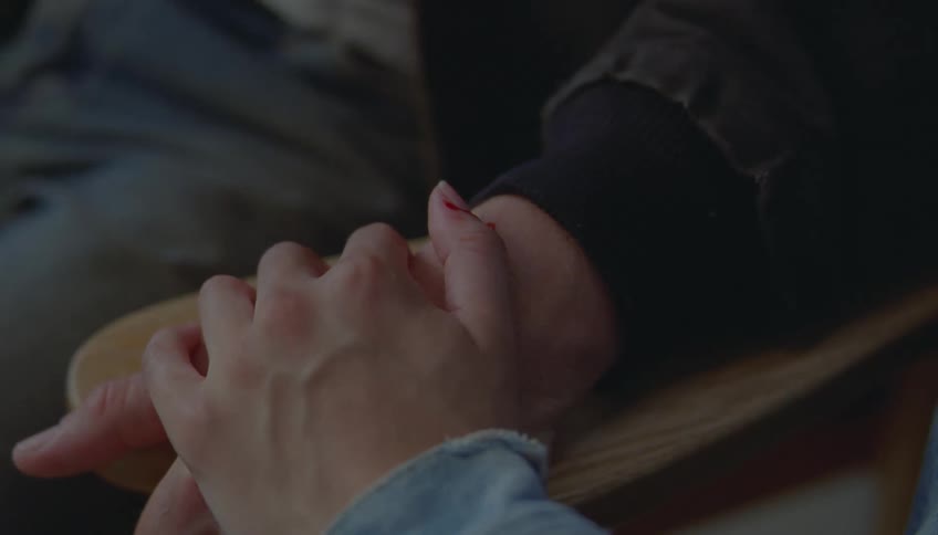 A close view of a woman holding the hand of a man with a small cut on his thumb as they sit together in a dimly lit room