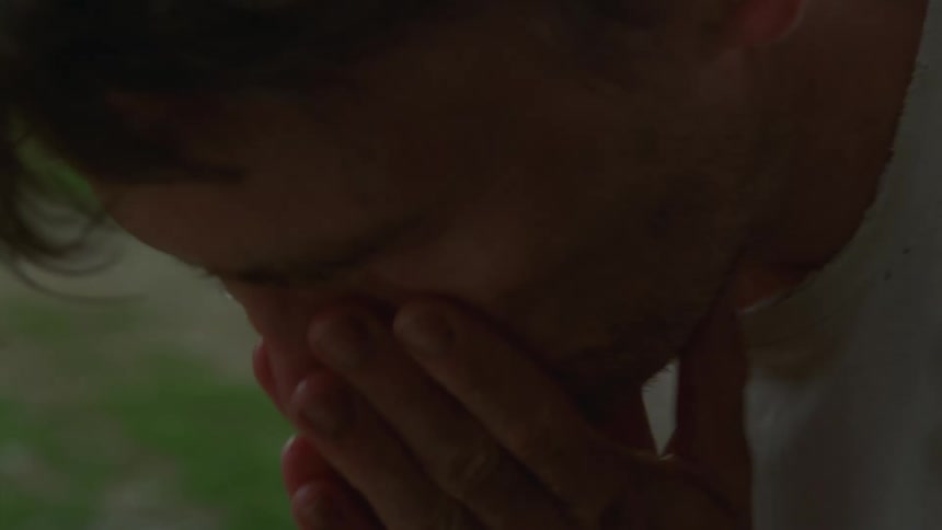 A close view of a man splashing water on his face outdoors while appearing tired and weathered