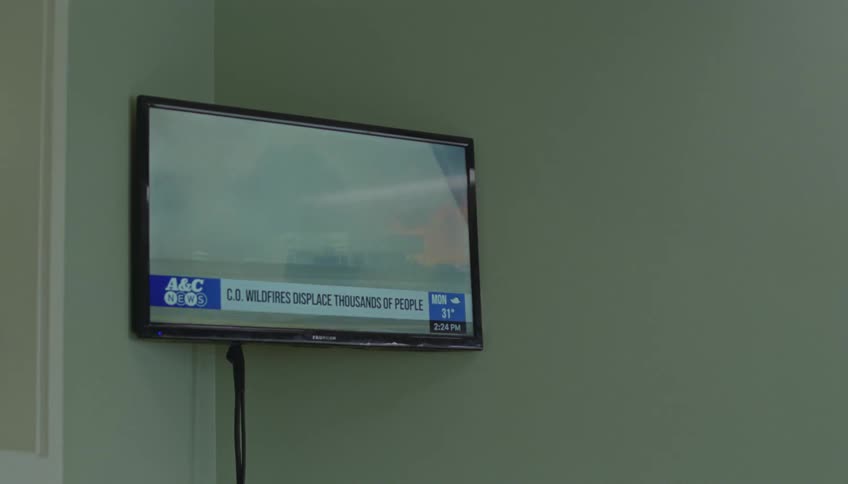 A wall mounted tv displays a news report about wildfires in a living room