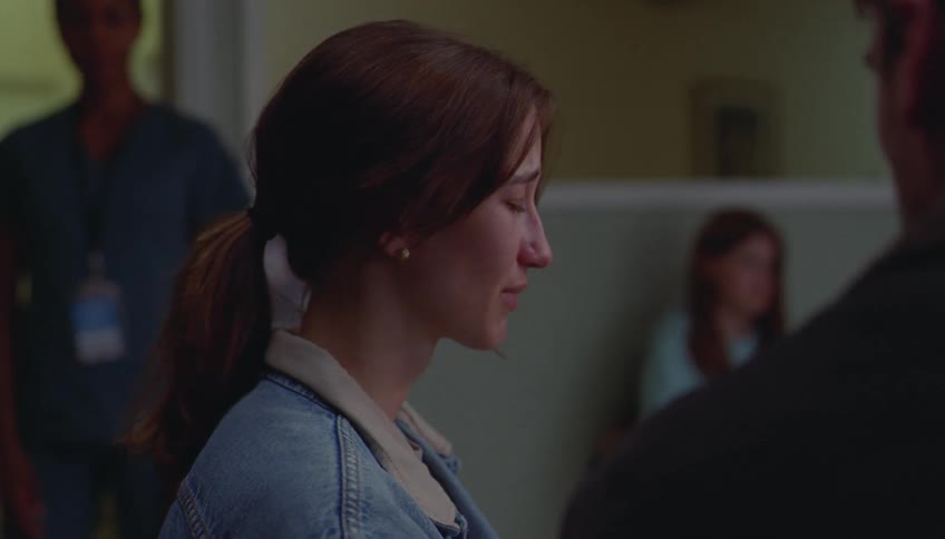 Woman frowns tearfully at her male companion before standing and following a medical professional