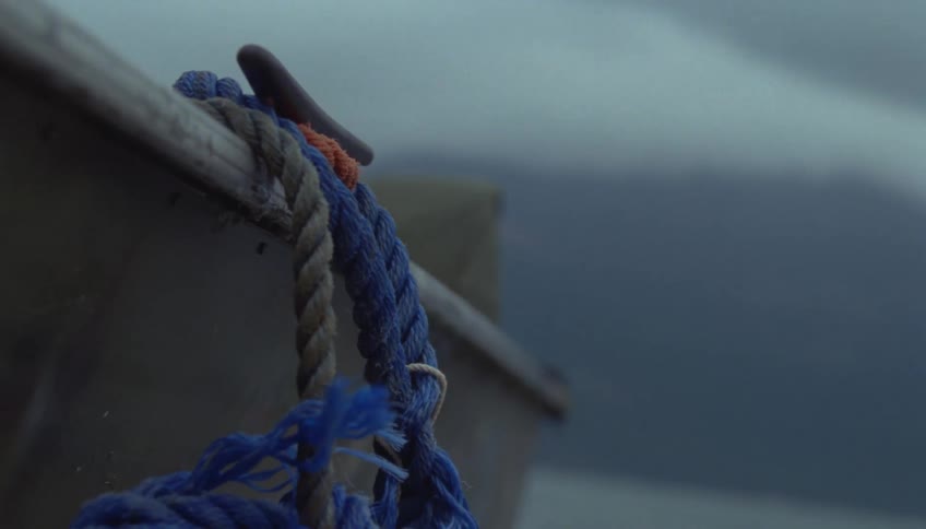 Blue rope tied to the side of a boat with sea and mountains blurred in the background