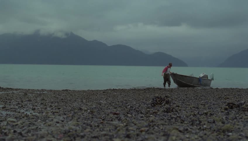 Man pulls a small motorboat onto the rock covered shore on a foggy day