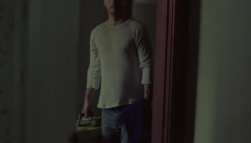 A man carrying a suitcase heads home walking through a doorway
