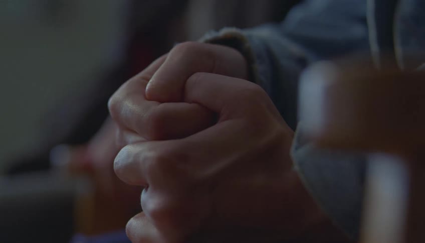 Two people sit indoors wearing jean jackets their hands gently linked between them the moment feels quiet and close