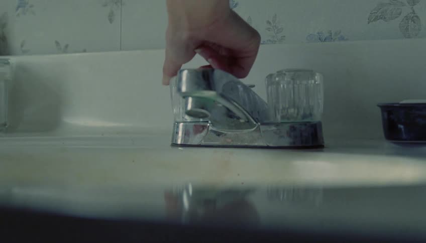 Hand turning a faucet knob on a bathroom sink