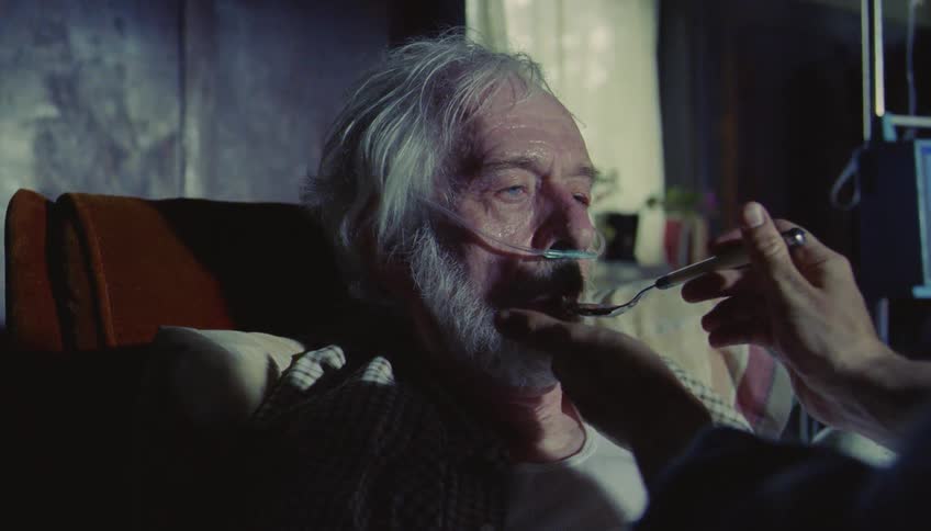 Elderly man being fed with a spoon while lying in a hospital setting