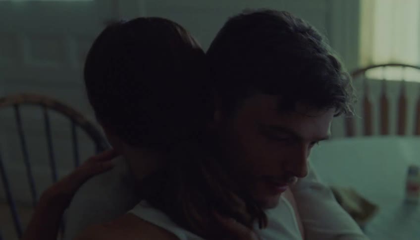 Person sitting while hugging another person in an indoor setting with soft light