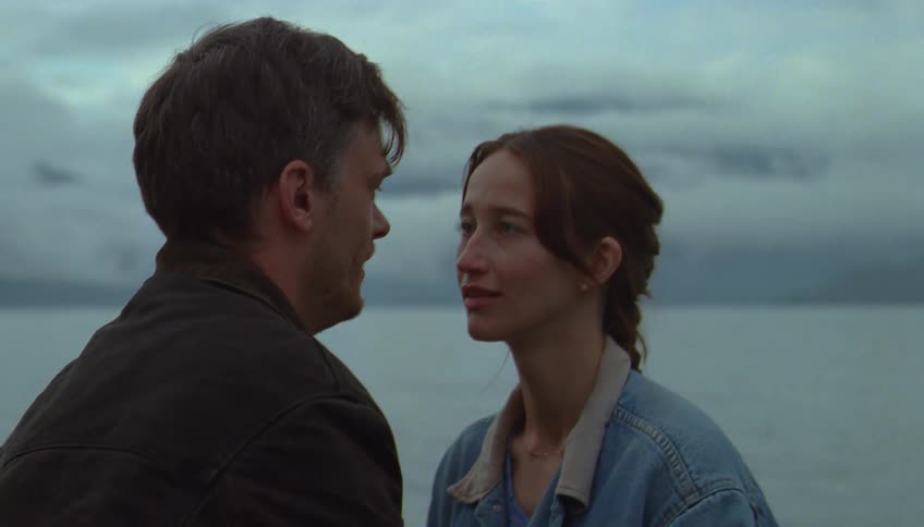 A man and a woman sit on a canoe in the ocean at midday staring at each other with quiet focused passion