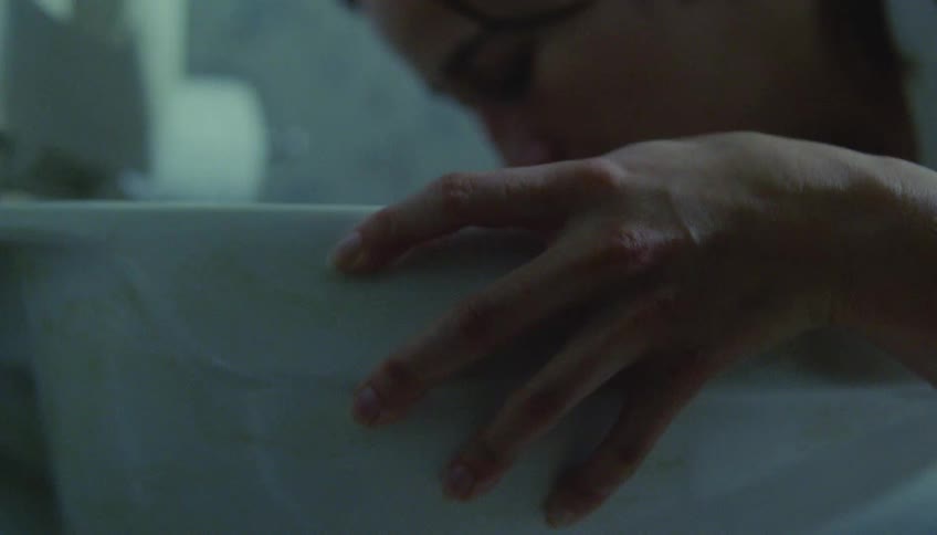 Young adult woman bending over a toilet while vomiting inside of it indoors