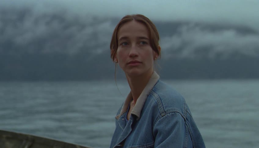 A woman sits quietly in a boat gazing thoughtfully across a dark misty lake at dusk