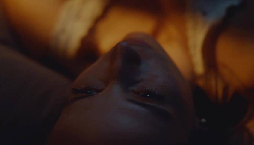 Female face lying down in closeup with eyes open under low light