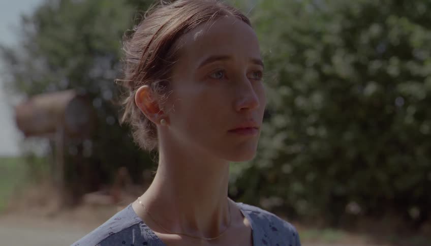 A woman gazes thoughtfully into the distance while standing outdoors in soft daylight
