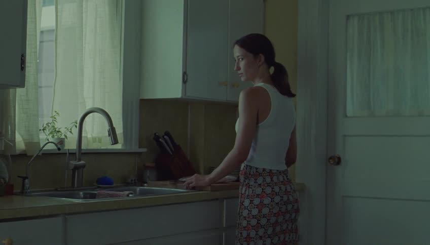Woman is standing in the kitchen with her hand resting on the counter looking back as a man sits down