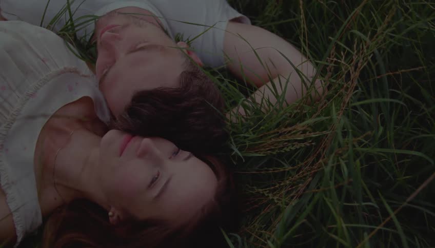 Couple lying on the grass with heads close together among the vegetation