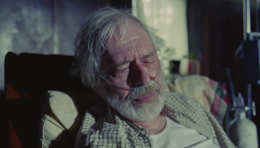 Man hugging an elderly patient lying in a hospital bed with medical equipment nearby