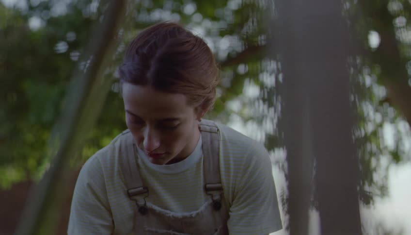 Woman wearing overalls working outdoors among trees