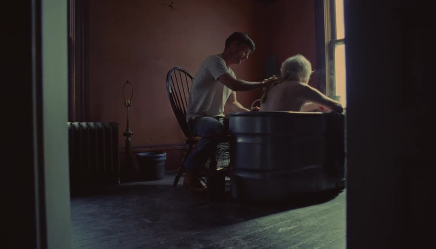 Man and woman assisting an elderly person during a bath in a tub inside a room