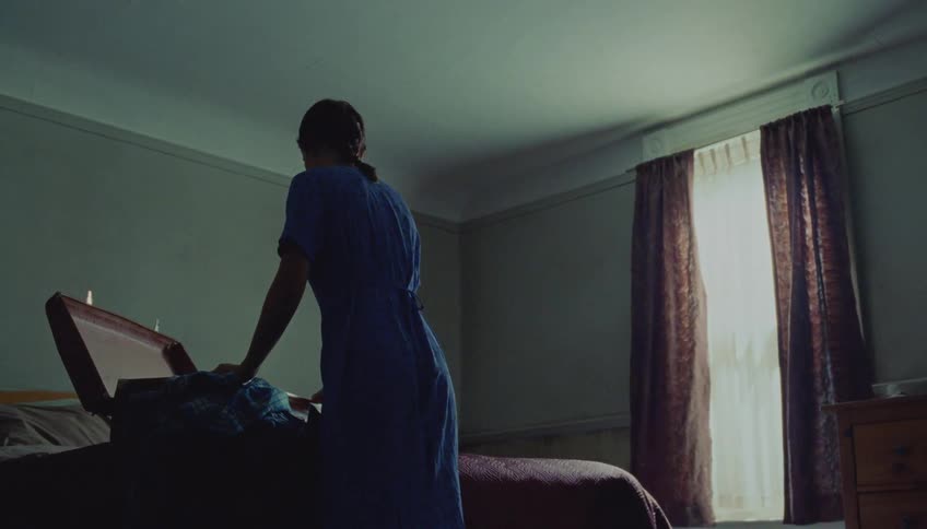 Woman in a bedroom arranging clothes inside an open suitcase on the bed